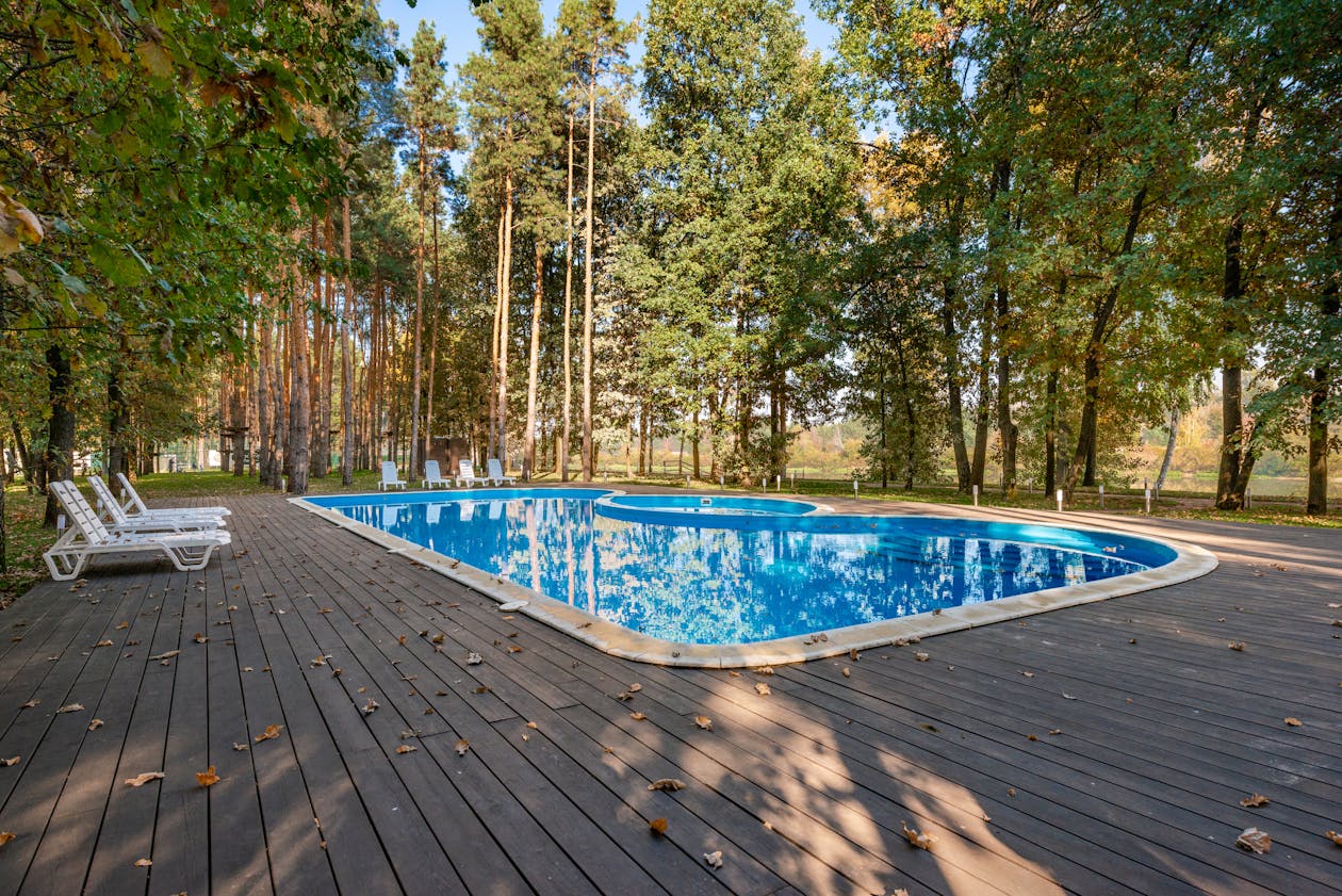 Serene outdoor pool deck with sun loungers amongst tall trees, ideal for a summer retreat. — pool deck coating Omaha