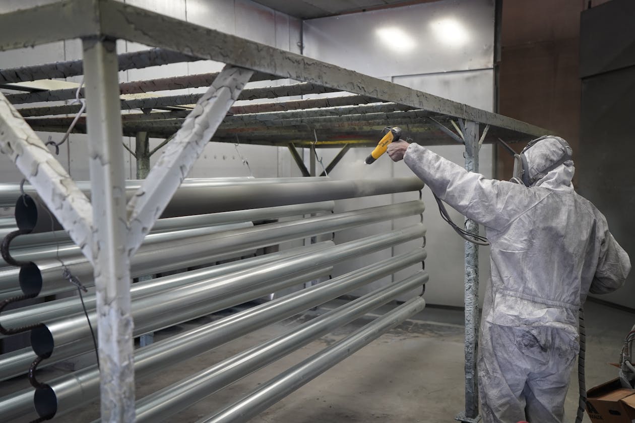 Technician applying powder coating to metal pipes in a workshop setting. — patio epoxy coating Omaha