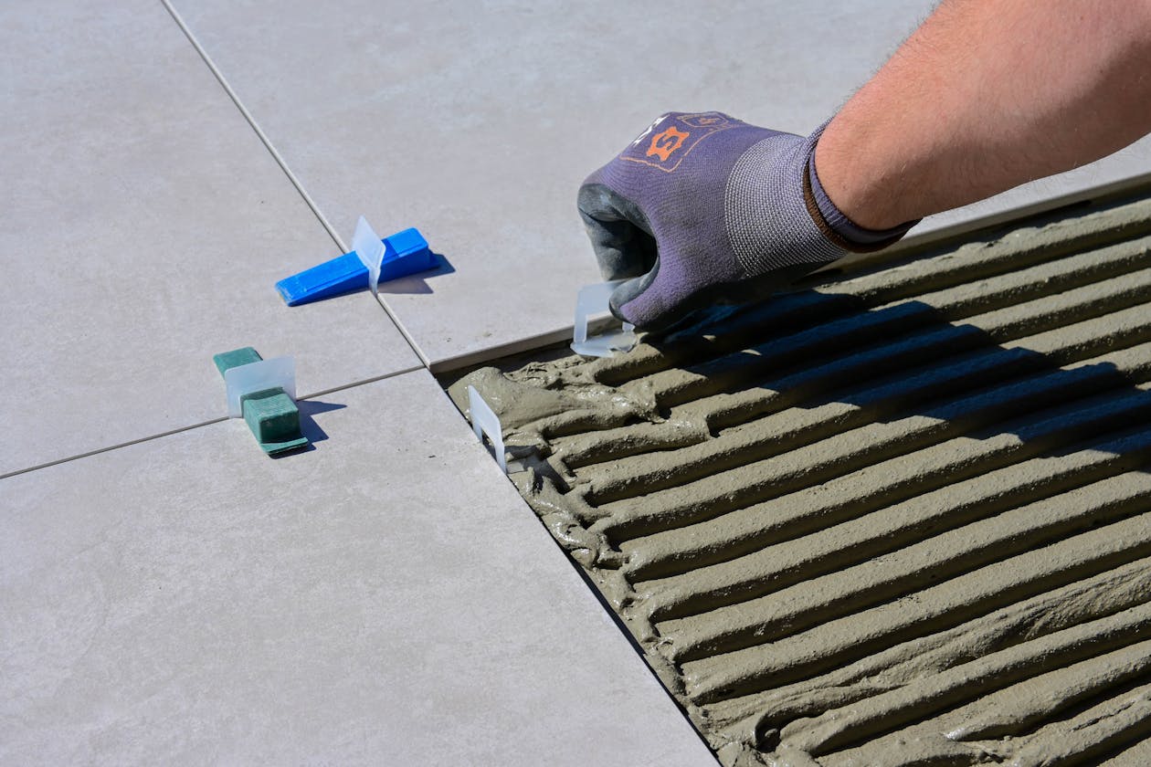 Detailed view of gloved hand aligning tiles with levelers and spacers during construction. — solid color epoxy flooring Omaha