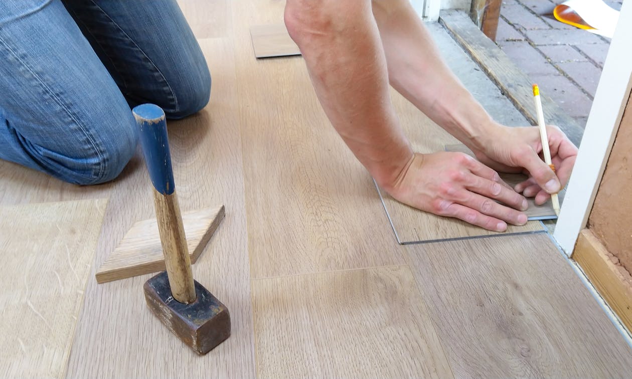 A craftsman carefully measures and marks wooden floor panels for precise installation. — epoxy flooring Benson